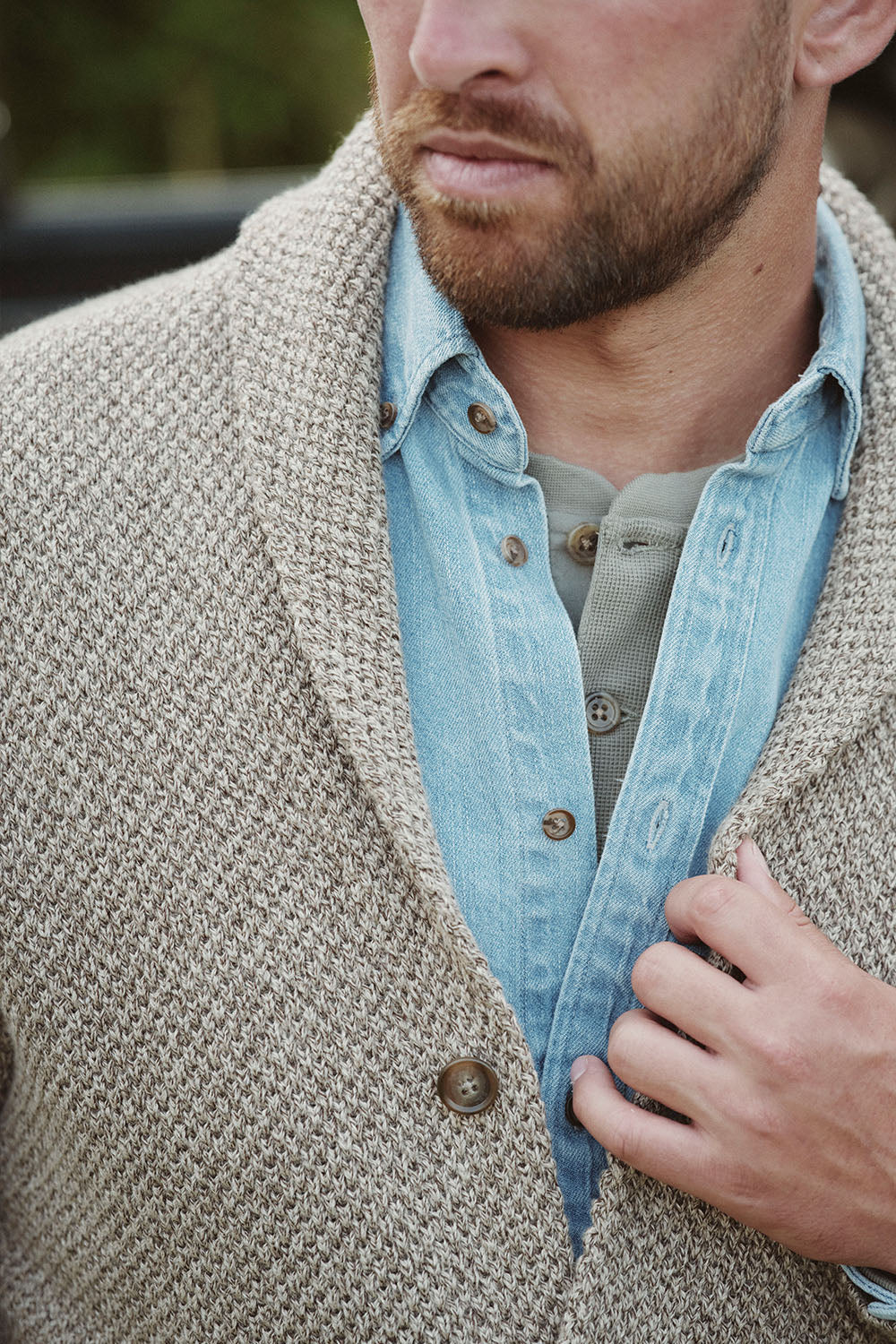 Man wearing a beige knit cardigan over a denim shirt, channeling effortless NZ style.