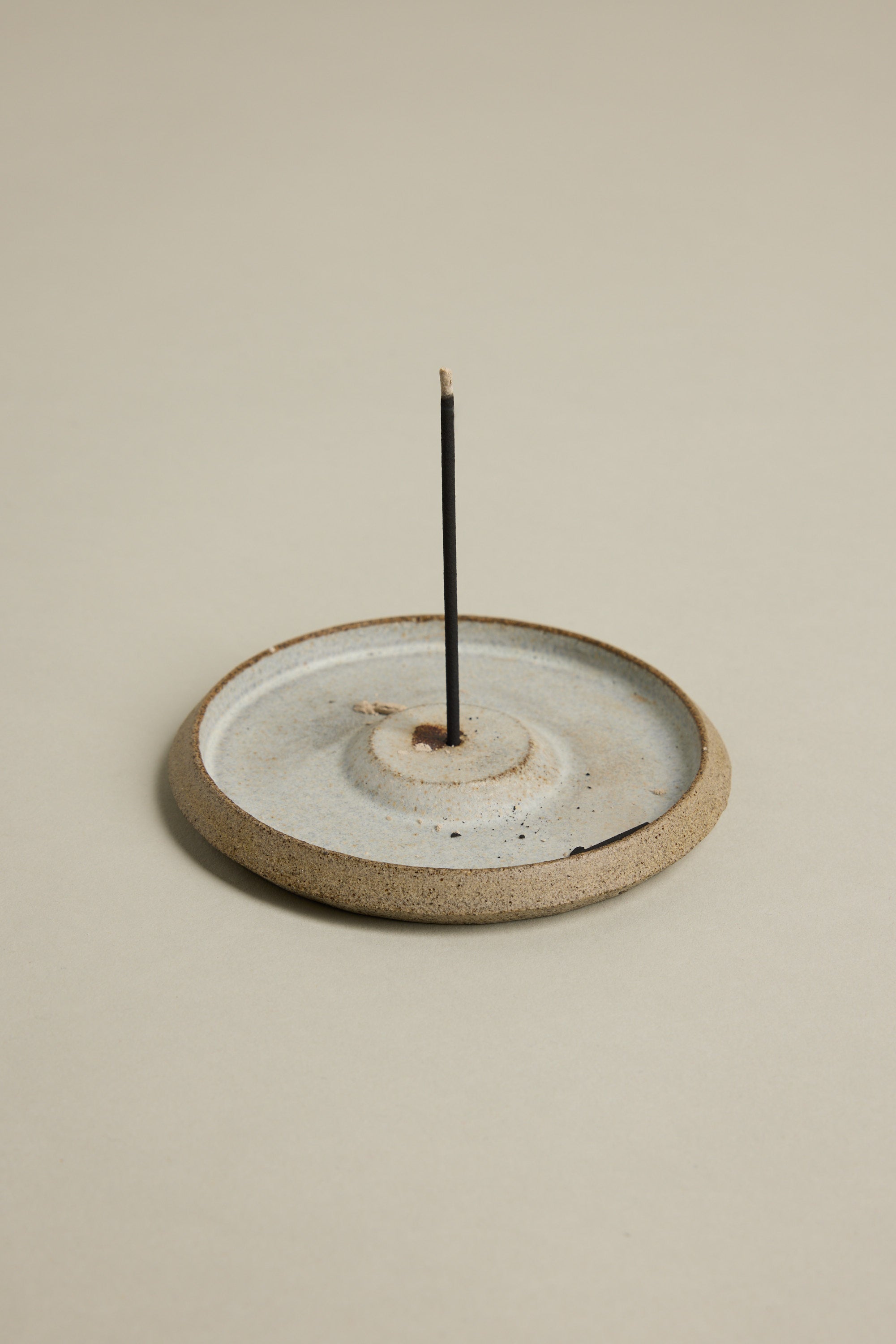 The Earl of East EoE Onsen Japanese Incense Stick stands upright, unlit, in a round ceramic holder with a shallow dish design against a neutral background.