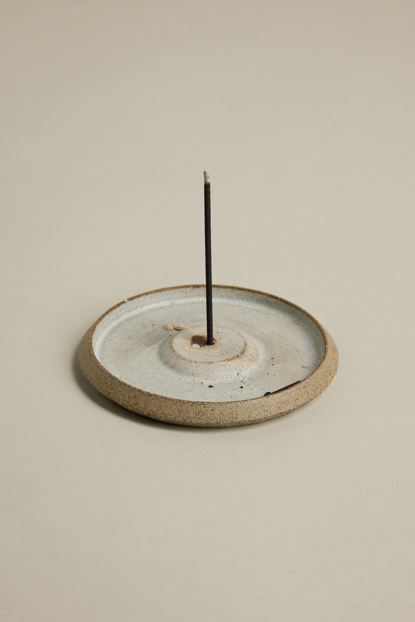 The Earl of East EoE Onsen Japanese Incense Stick stands upright, unlit, in a round ceramic holder with a shallow dish design against a neutral background.