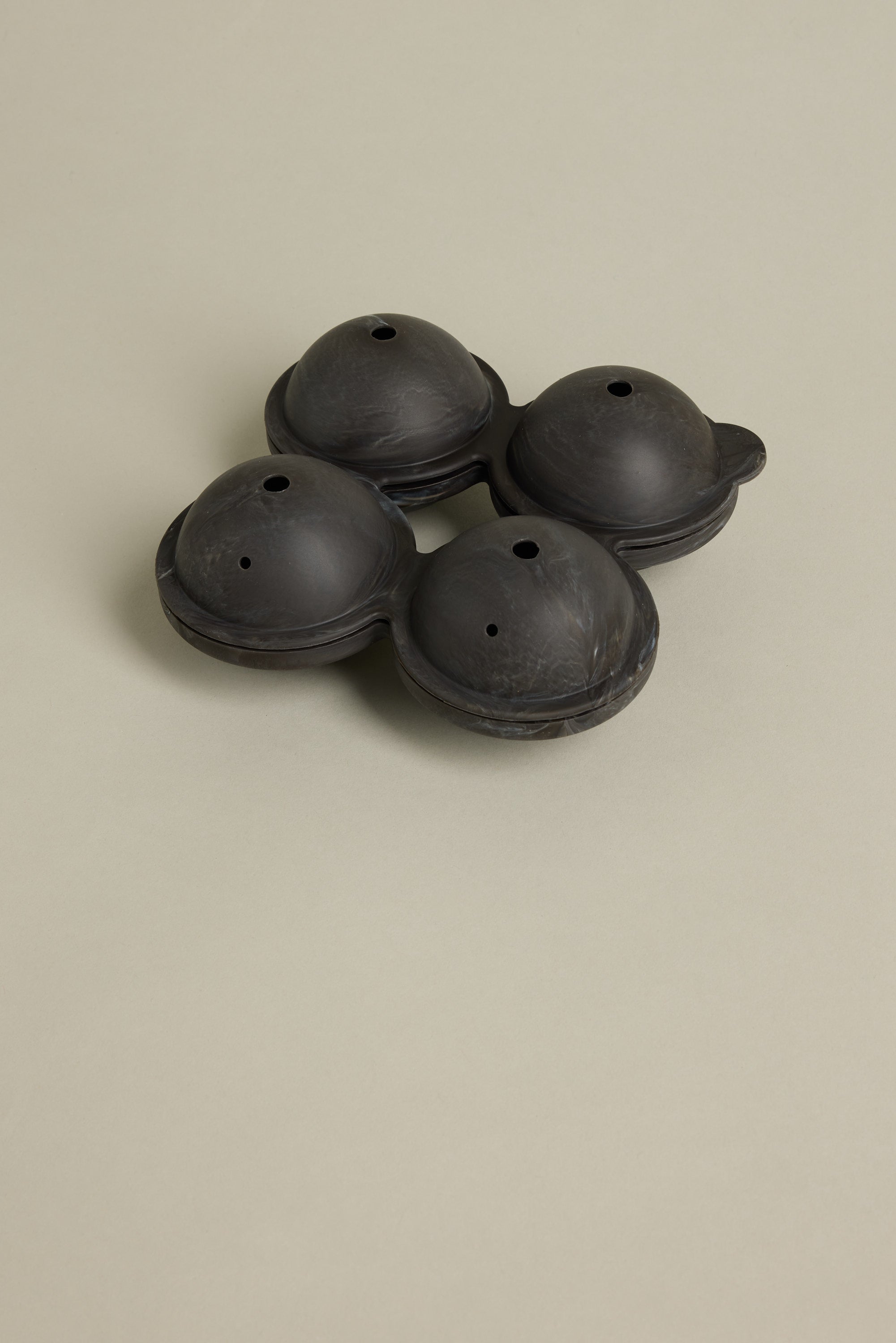 The Barkers Ice Tray Sphere Marble Black features four compartments and small top holes, ideal for crafting large round ice spheres—perfect for cocktails. Displayed here on a plain light beige surface.