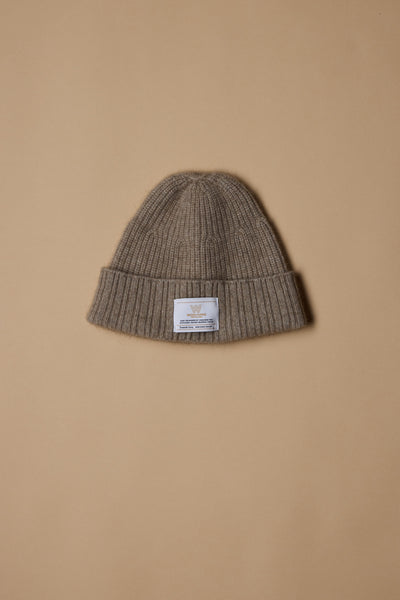 The NZ Made Perino Beanie by Woolyarns Perino is a brown ribbed knit merino possum silk blend beanie with a folded cuff and white label, shown on a beige background—crafted in New Zealand for stylish warmth.