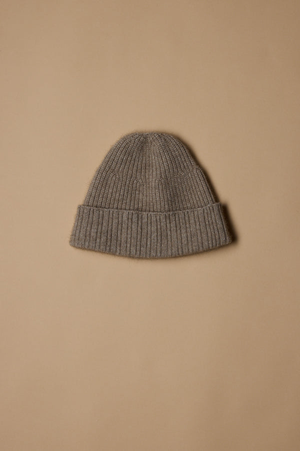 The Woolyarns Perino NZ Made Perino Beanie, in gray and crafted from a luxurious merino possum silk blend, features a folded brim and is displayed on a plain light brown background.