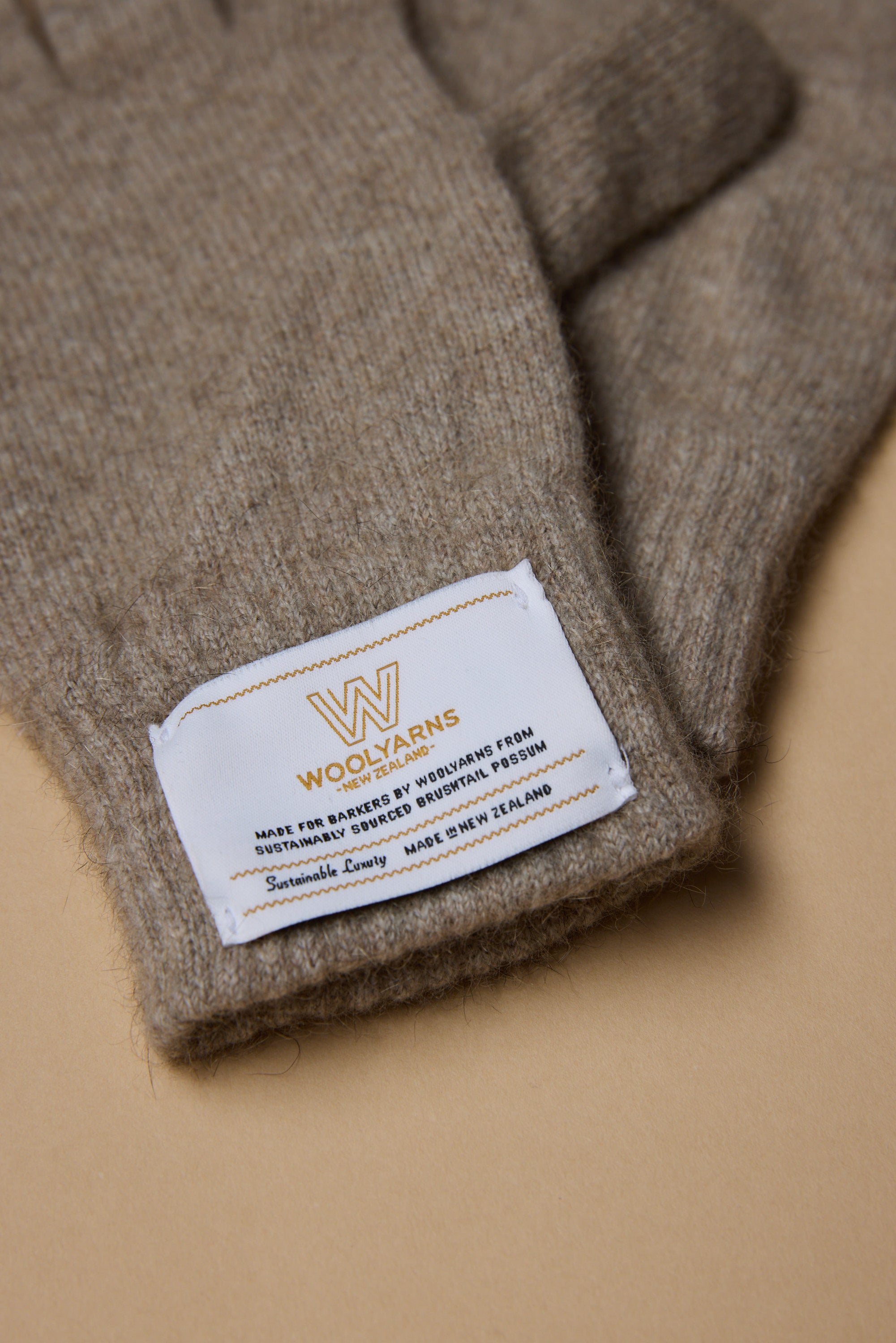 A close-up of NZ Made Perino Gloves by Woolyarns Perino, featuring a white fabric label and crafted from sustainable, biodegradable merino wool in beige.