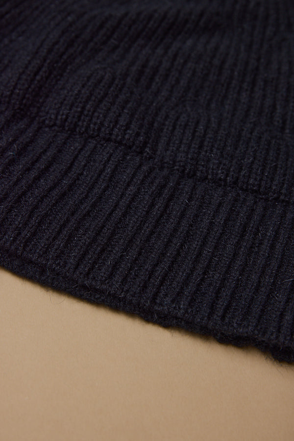 Close-up of a black ribbed knit fabric from the Woolyarns Perino NZ Made Perino Beanie, laid on a light brown surface. The texture and stitching detail highlight the premium quality of New Zealand made merino possum silk.