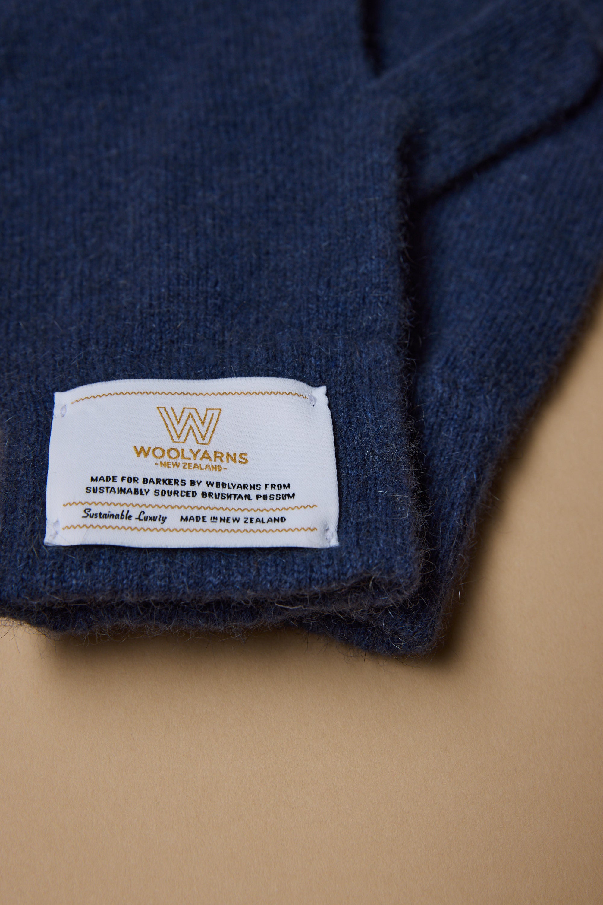A close-up of Woolyarns Perino NZ Made Perino Gloves showcases their premium merino possum silk blend and white WOOLYARNS label, reflecting sustainable New Zealand craftsmanship on a light brown surface.