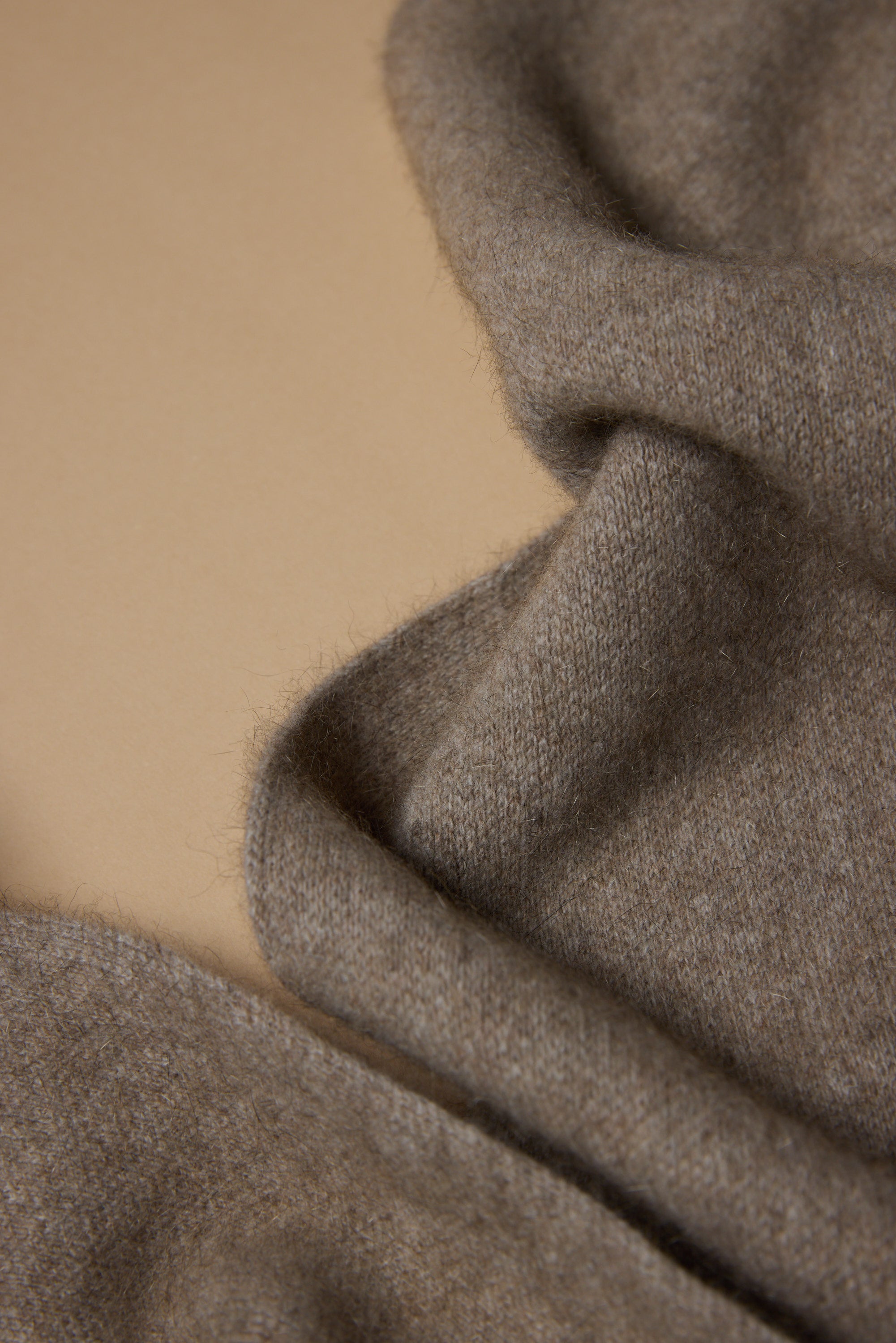 A close-up of soft, light brown merino possum silk blend wool, slightly fuzzy and casually draped on beige—highlighting the NZ Made Perino Scarf by Woolyarns Perino.