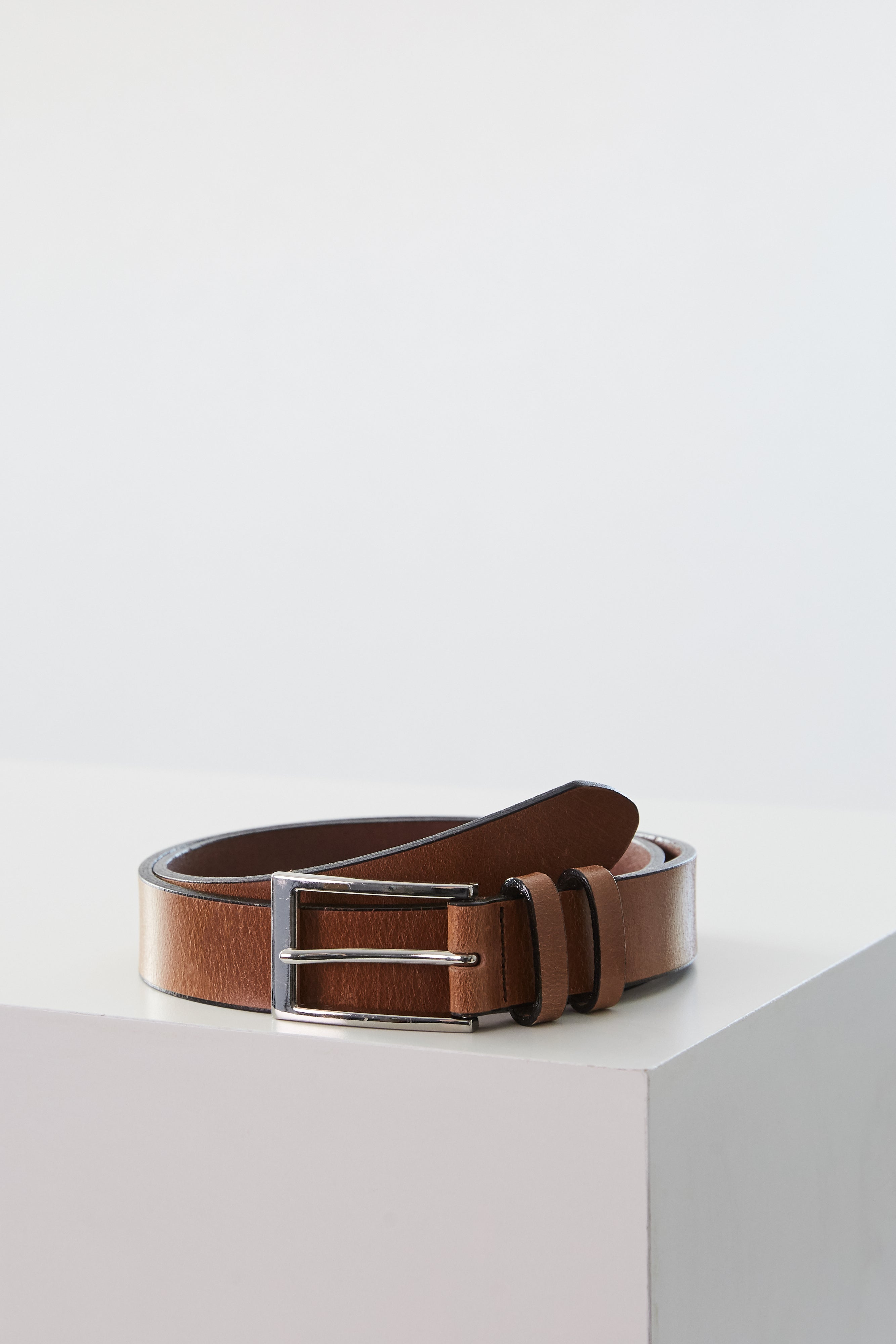 The Barkers Frances Leather Belt, featuring a brown leather strap and square buckle, is coiled neatly on a white surface with a plain light background.