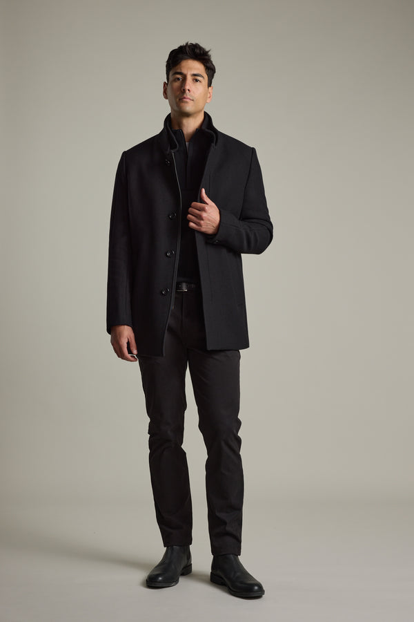 Man in black Barkers Raymond Coat, black pants, and shoes stands against a plain background.