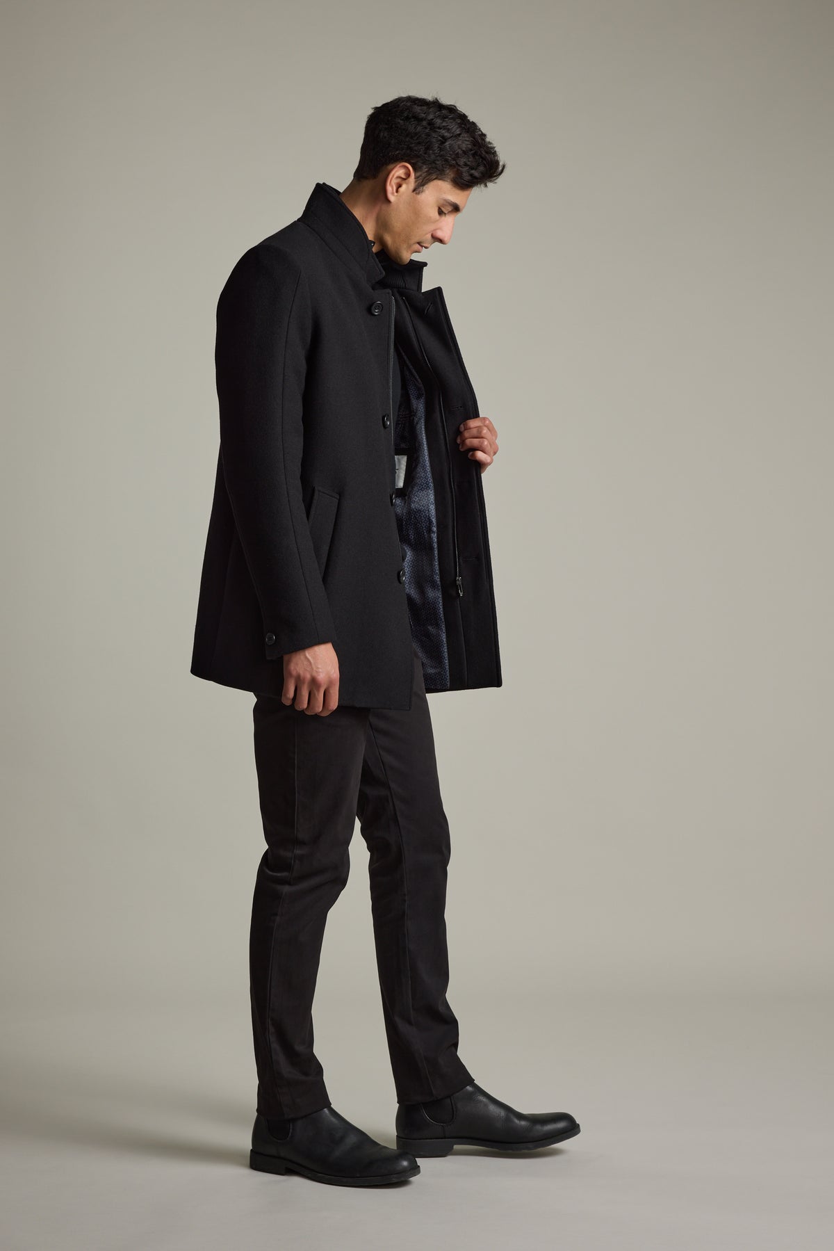 Man in Barkers Raymond Coat, black pants & boots, looks down while opening his coat.