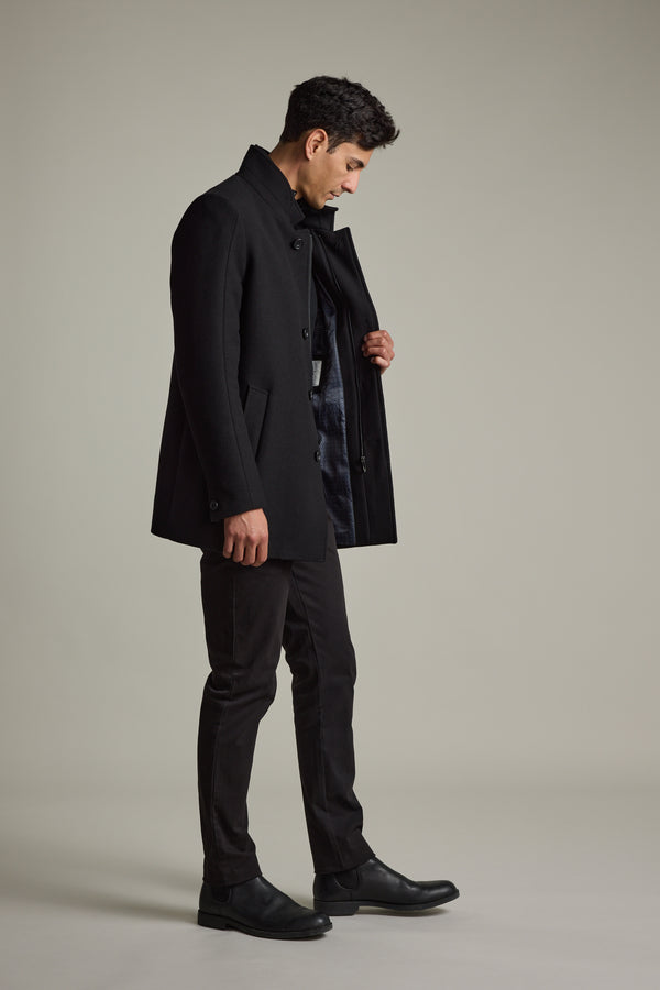 Man in Barkers Raymond Coat, black pants & boots, looks down while opening his coat.