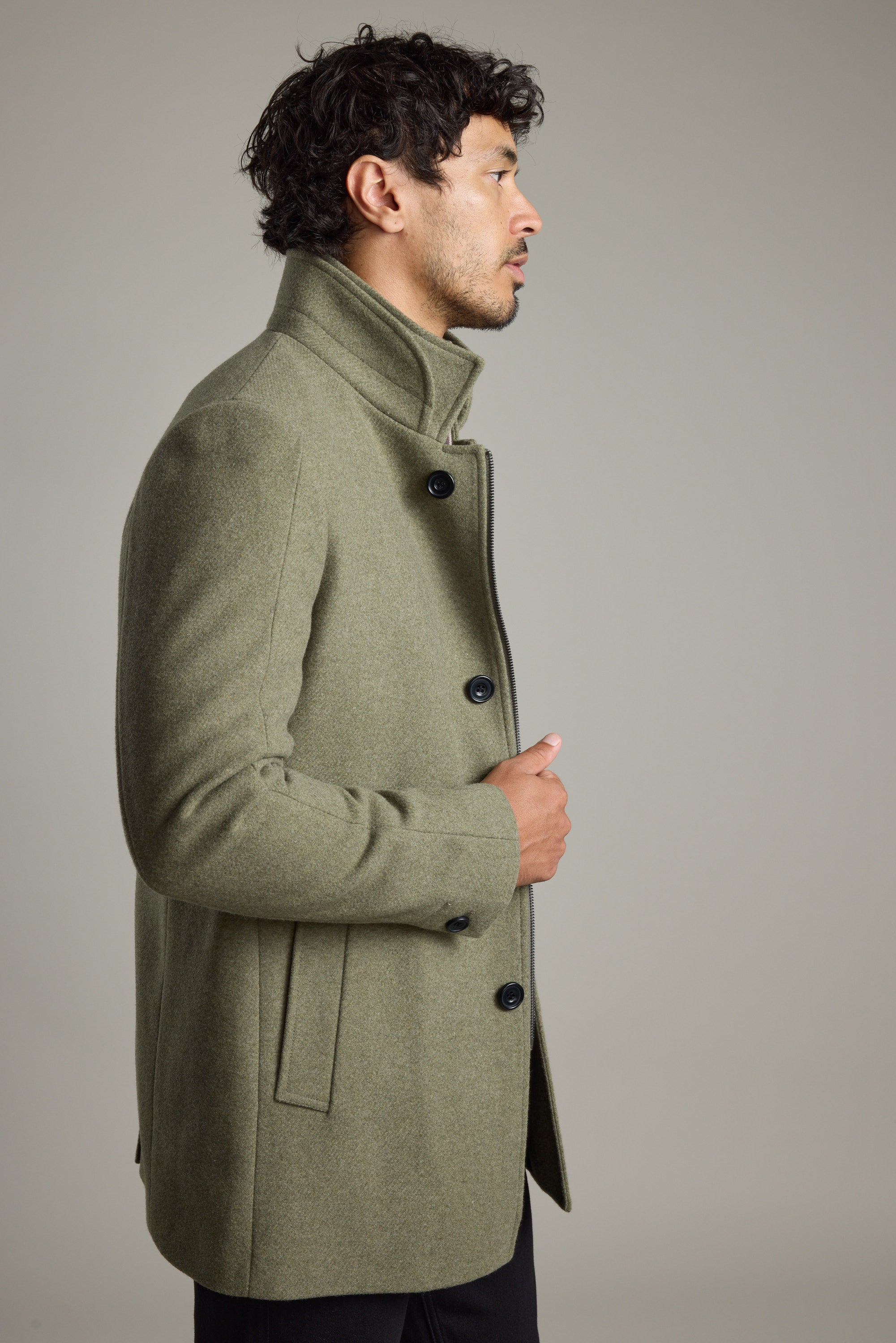 Man in a green Barkers Raymond Coat stands sideways against a plain grey background.