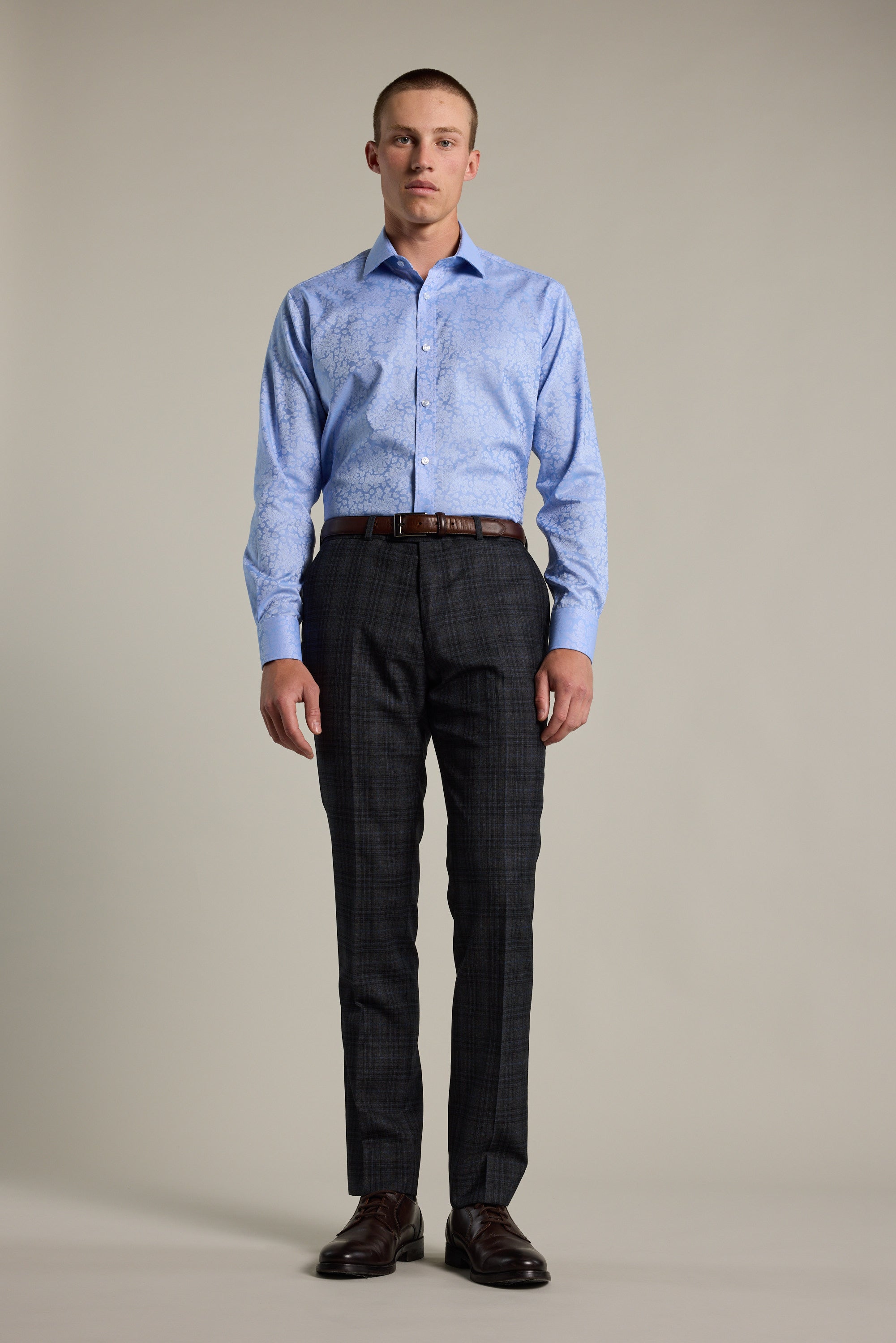 A man stands facing forward in a Barkers Corran Paisley Business Shirt, paired with dark plaid dress pants, a brown belt, and dark brown dress shoes, set against a plain neutral background.