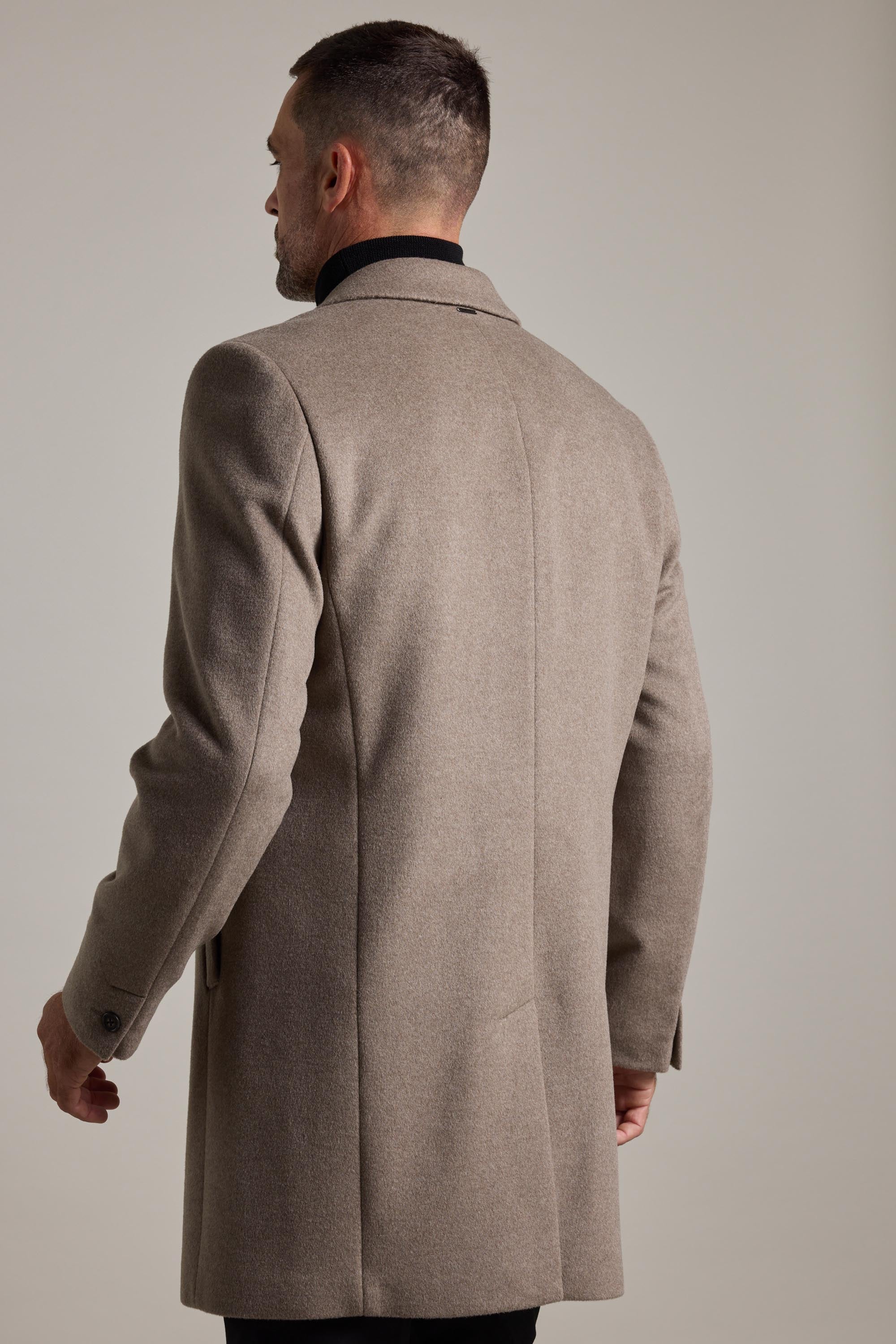 A man with short hair is seen from behind wearing a light brown Barkers Morrison Coat, a tailored wool blend, over a black shirt against a plain light background.