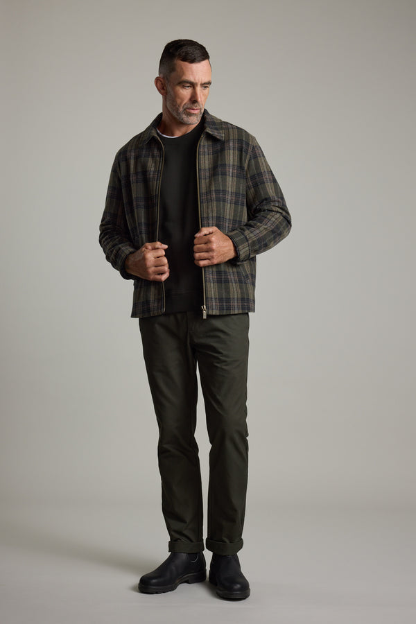 Man in Barkers Zermatt Wool Jacket, dark pants, and boots stands before a light gray background.