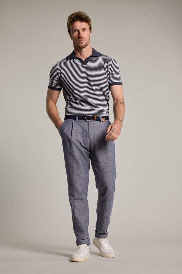 A man with short hair and a trimmed beard poses with his hands in his pockets, wearing the Barkers Parkway Cotton Stripe Polo, blue pleated belted trousers, and white sneakers against a plain background.