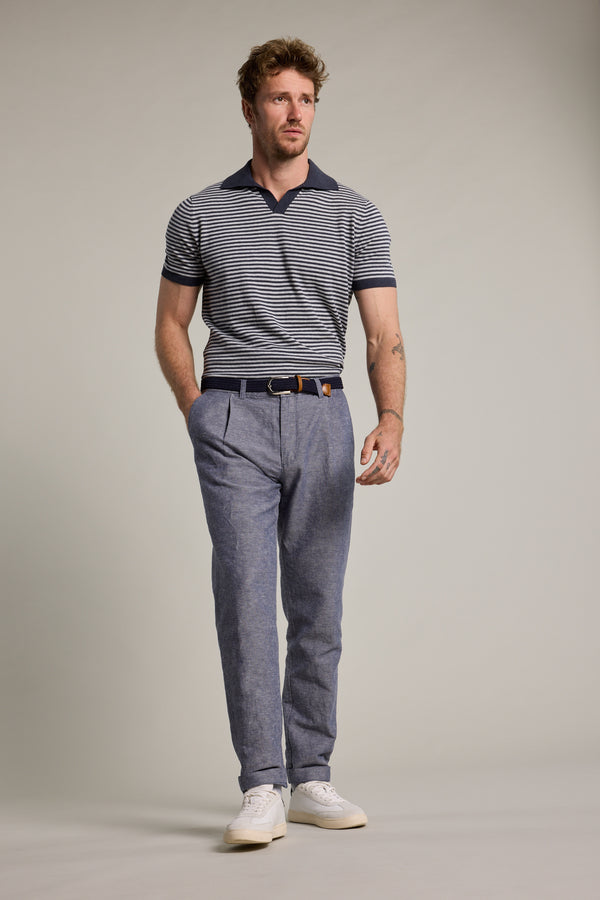 A man with short brown hair and a beard wears a navy striped polo, Barkers Newman Linen Pants, a dark belt, and white sneakers, standing against a plain light gray background.