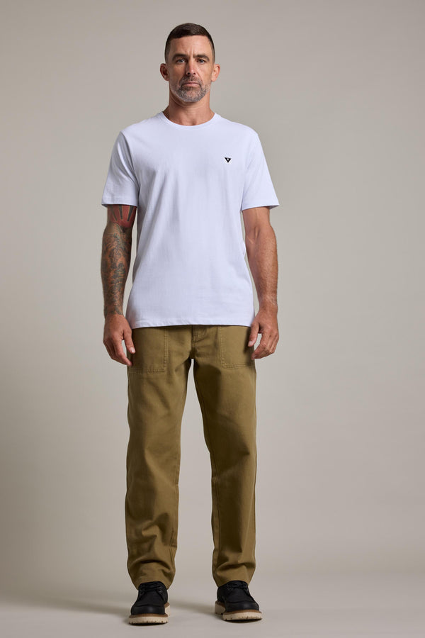 A man with short hair and a mustache faces forward, wearing a plain white T-shirt, Barkers Midwood Fatique Pant in olive green, and black shoes. He has visible tattoos on his left arm, with a plain light-colored background.