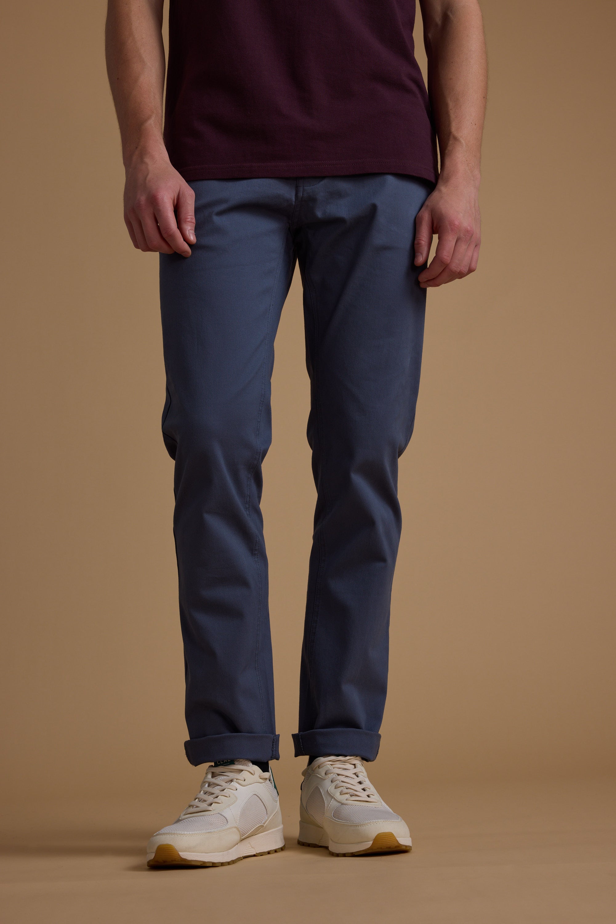 Only the lower half of a person in a maroon shirt, white sneakers, and Barkers Beckett 5-Pocket Pant is visible as they stand against a plain beige background.