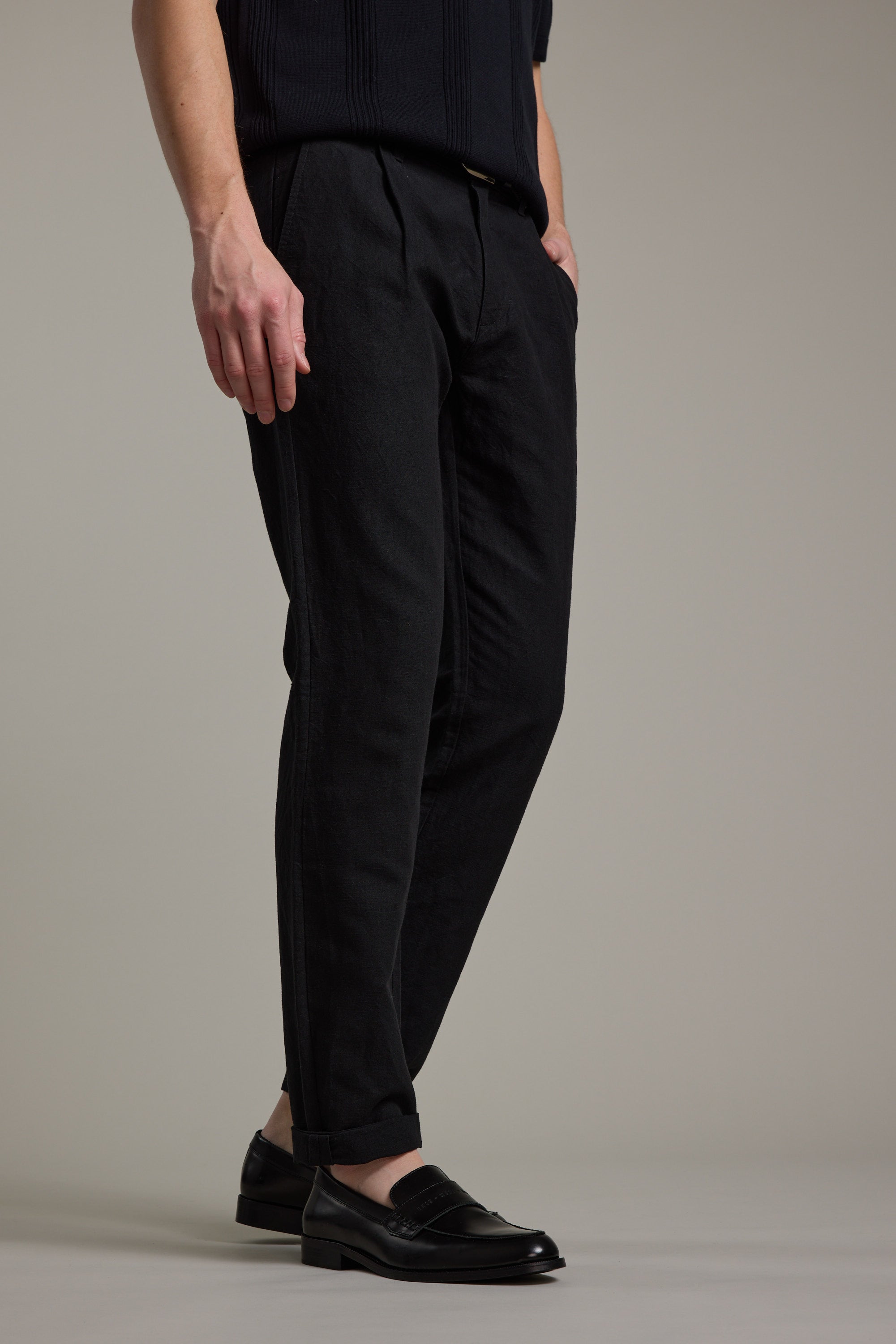 A person models the Barkers Newman Linen Pant in black with black loafers, standing against a plain light gray background; only the lower half of their body is shown, hands in pockets.