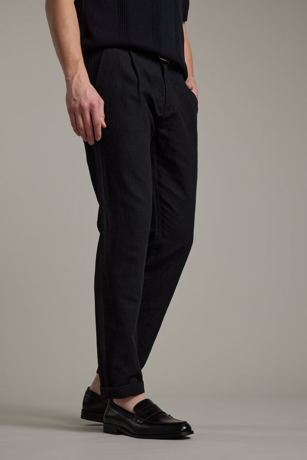 A person models the Barkers Newman Linen Pant in black with black loafers, standing against a plain light gray background; only the lower half of their body is shown, hands in pockets.
