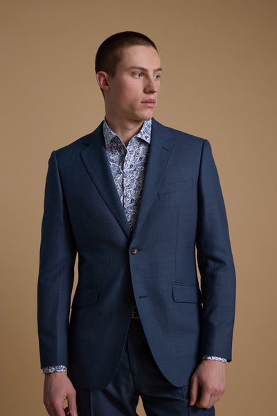 A man models the Barkers Morden Texture Suit Jacket with a patterned shirt, standing against a beige background and gazing slightly left with a neutral expression.