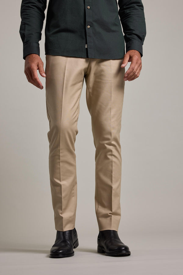 A person in Barkers' Lyndon Cotton Pants (beige), a dark green button-up shirt, and black dress shoes stands against a plain light background. The smart casual image is cropped at the shoulders.