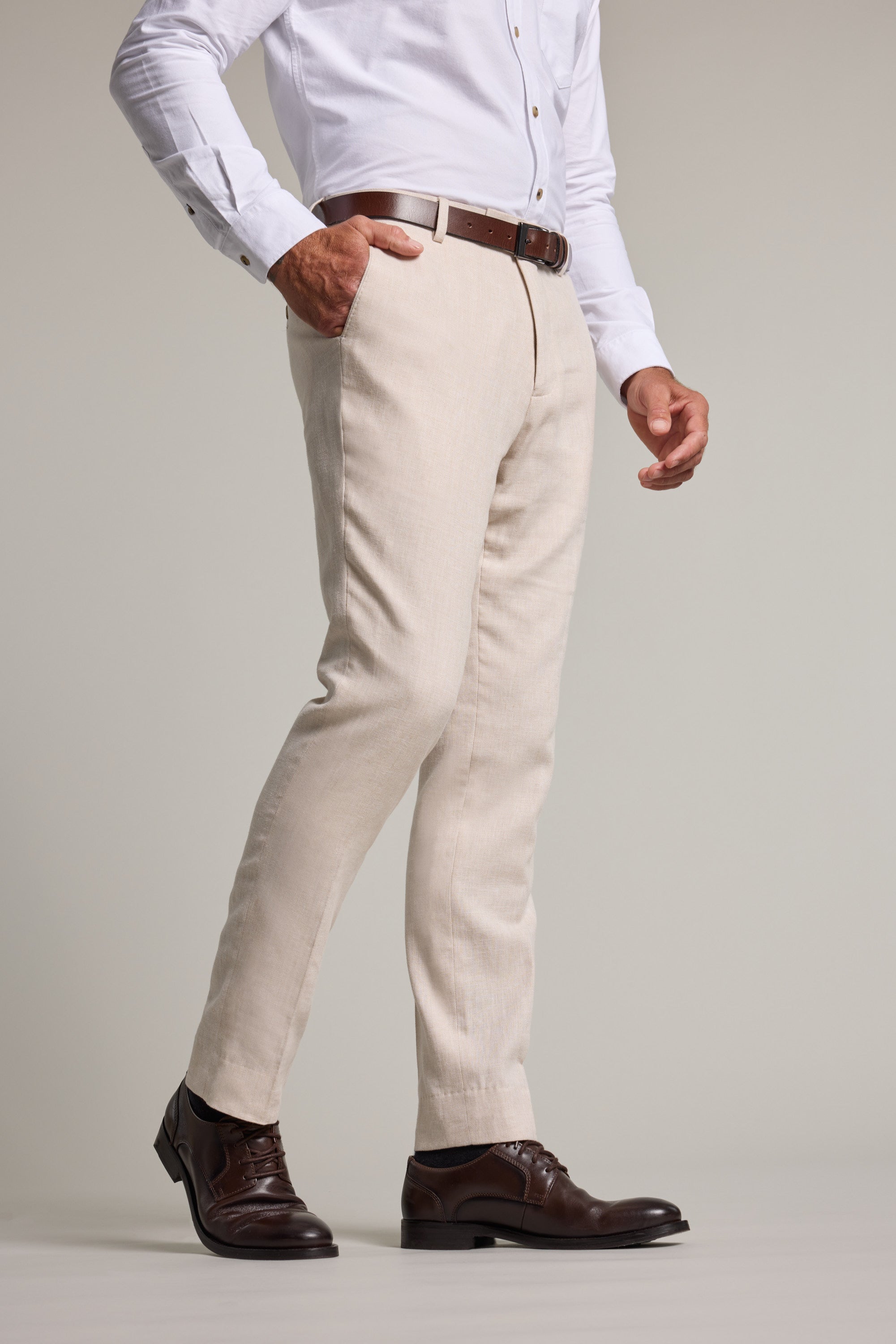 A man wears Barkers Thompson Textured Linen Pant in beige, white shirt, brown belt, and shoes.