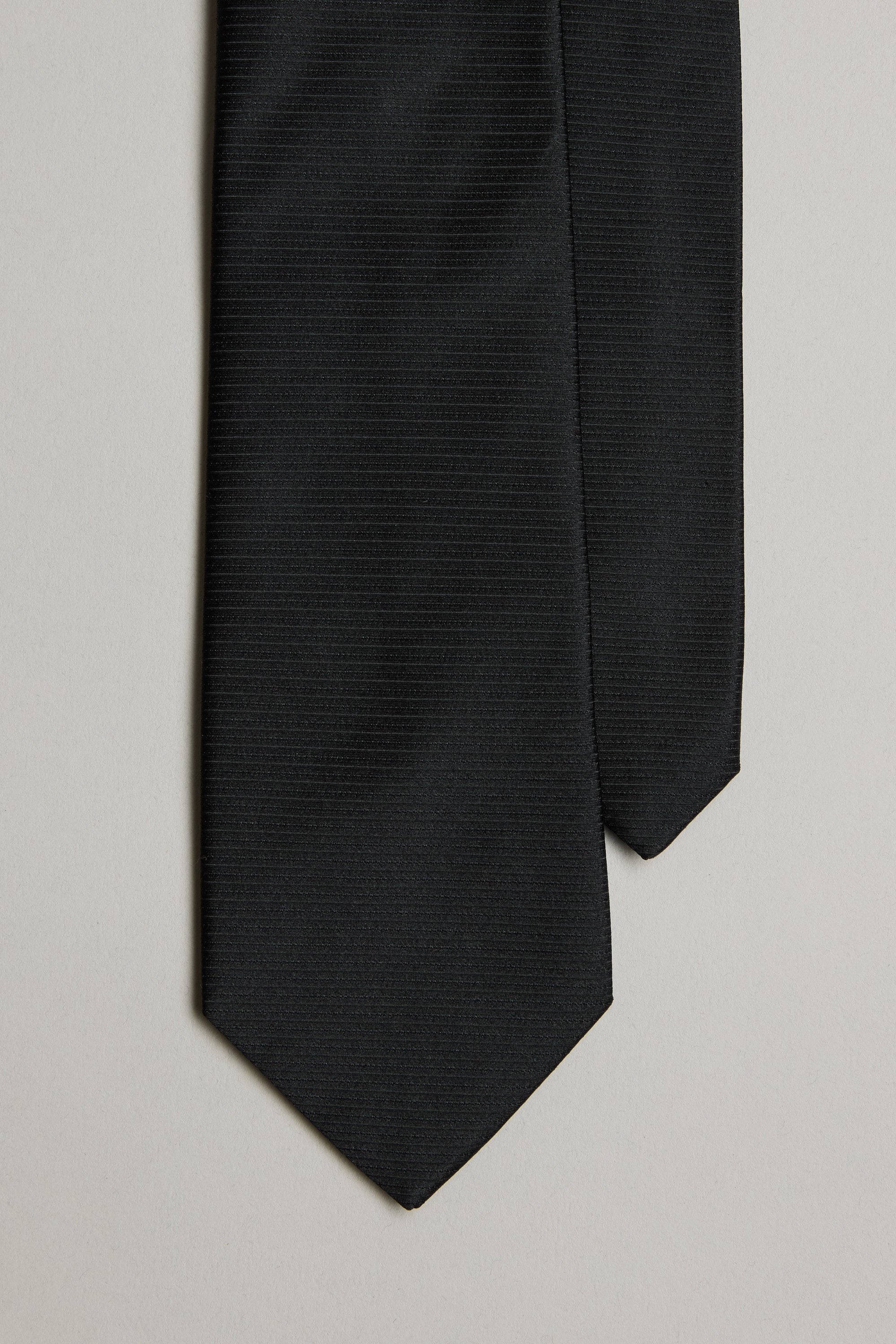 A close-up of the Barkers Black Tie features its subtle jacquard print on the bottom ends, set against a light gray background.