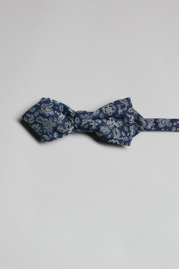 The Parisian Floral Bow Tie by Parisian, featuring a blue paisley pattern, is laid flat on a light gray background with its adjustable neck strap extended to the right.