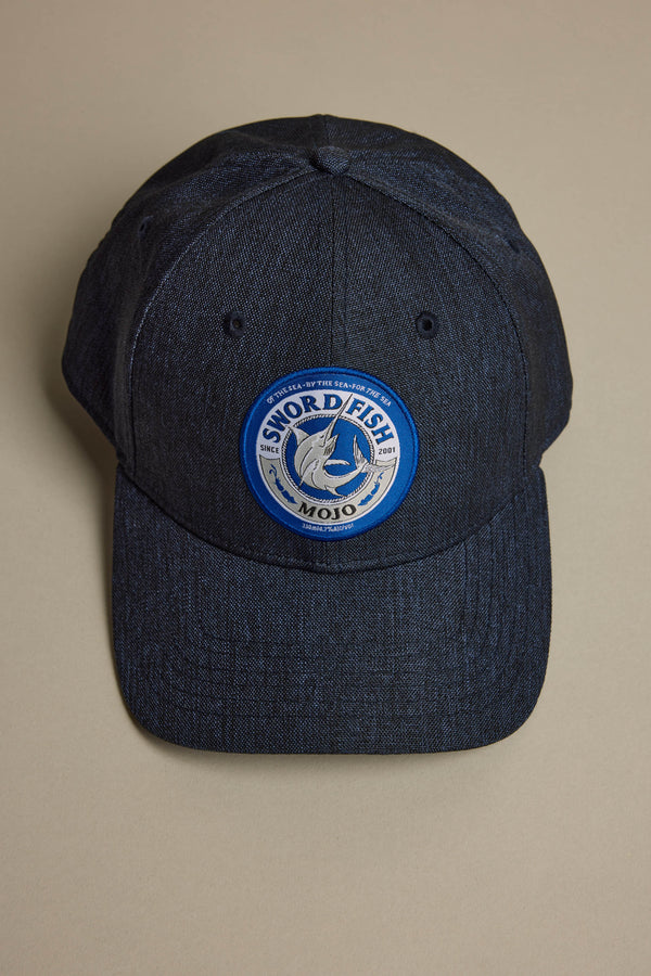 The Swordfish Mojo Trucker Cap by Swordfish Mojo features dark denim, a round blue and white patch with a swordfish image and "Sword Fish Mojo" text. Part of the exclusive merch collection, it's shown on a neutral background.