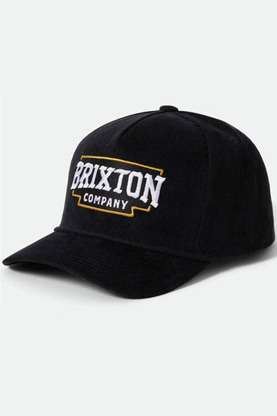 The Brixton Pierson Snapback is a black cotton corduroy hat with a curved brim, featuring bold white "BRIXTON" and smaller "COMPANY" text framed in yellow on the front. An adjustable snapback offers a comfortable fit.