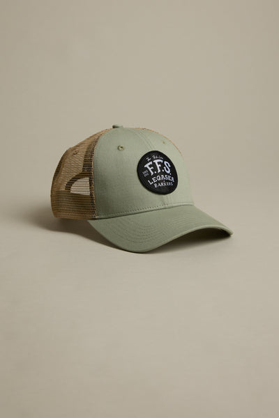 The Legasea FFS Trucker Cap features green and tan mesh with a black patch that reads "FFS Legacy Eager" in white. Displayed on a beige background, it's perfect for Legasea fans.