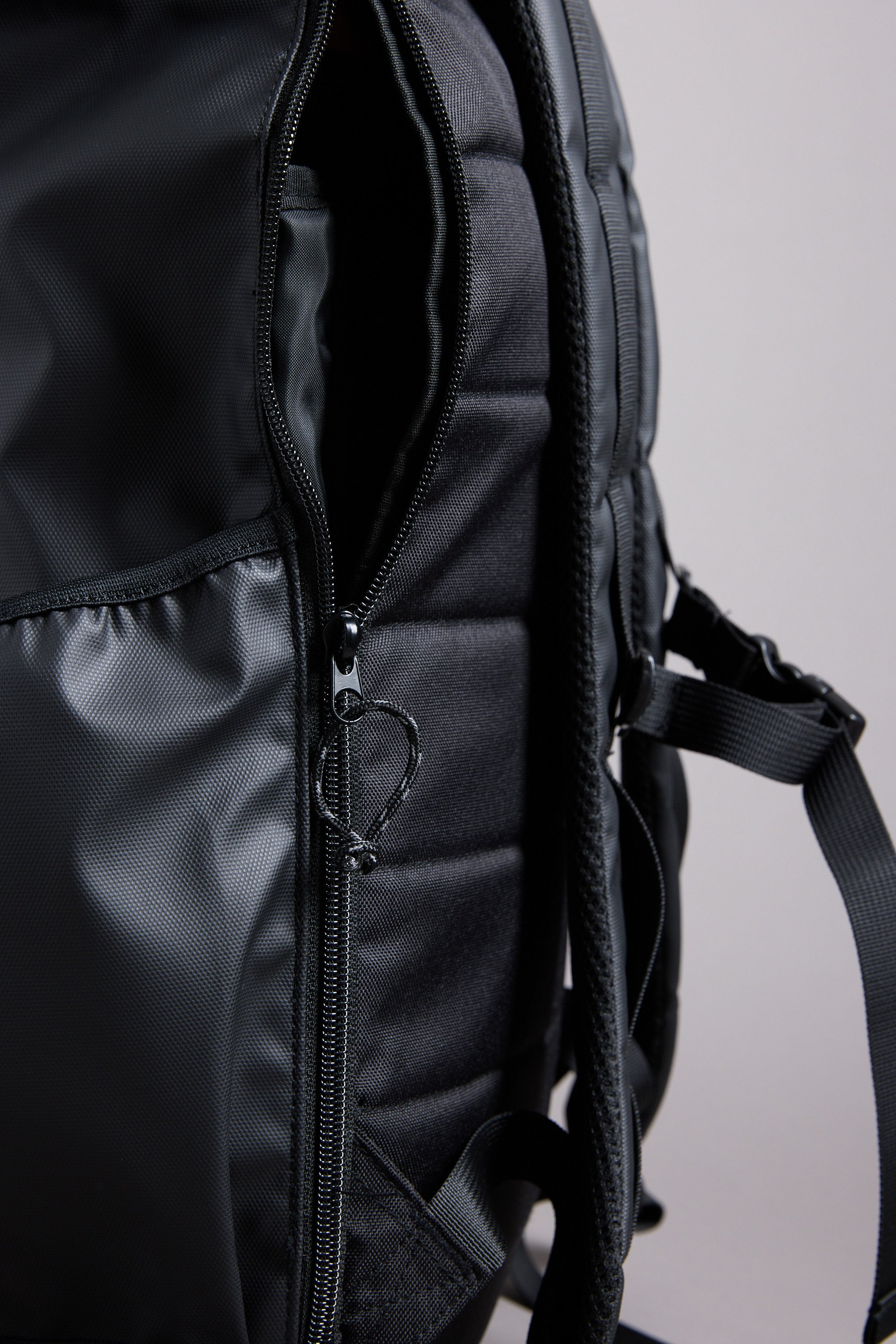 Close-up of the WearEver Transit Backpack by WearEver, featuring a partially unzipped water-resistant pocket, padded back panel, shoulder strap, and side pocket against a plain background.