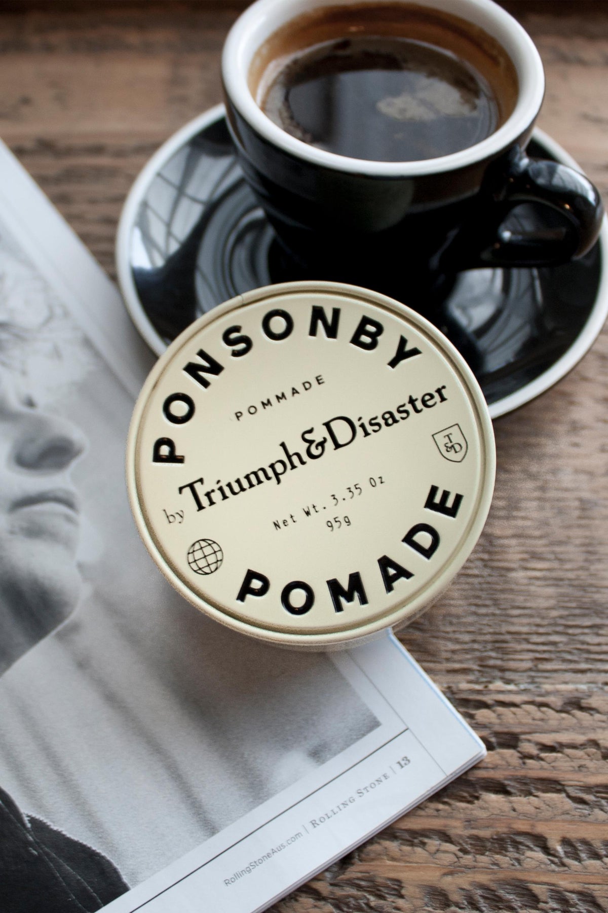 A coffee and Triumph & Disaster Ponsonby Pomade on a magazine with a photo.