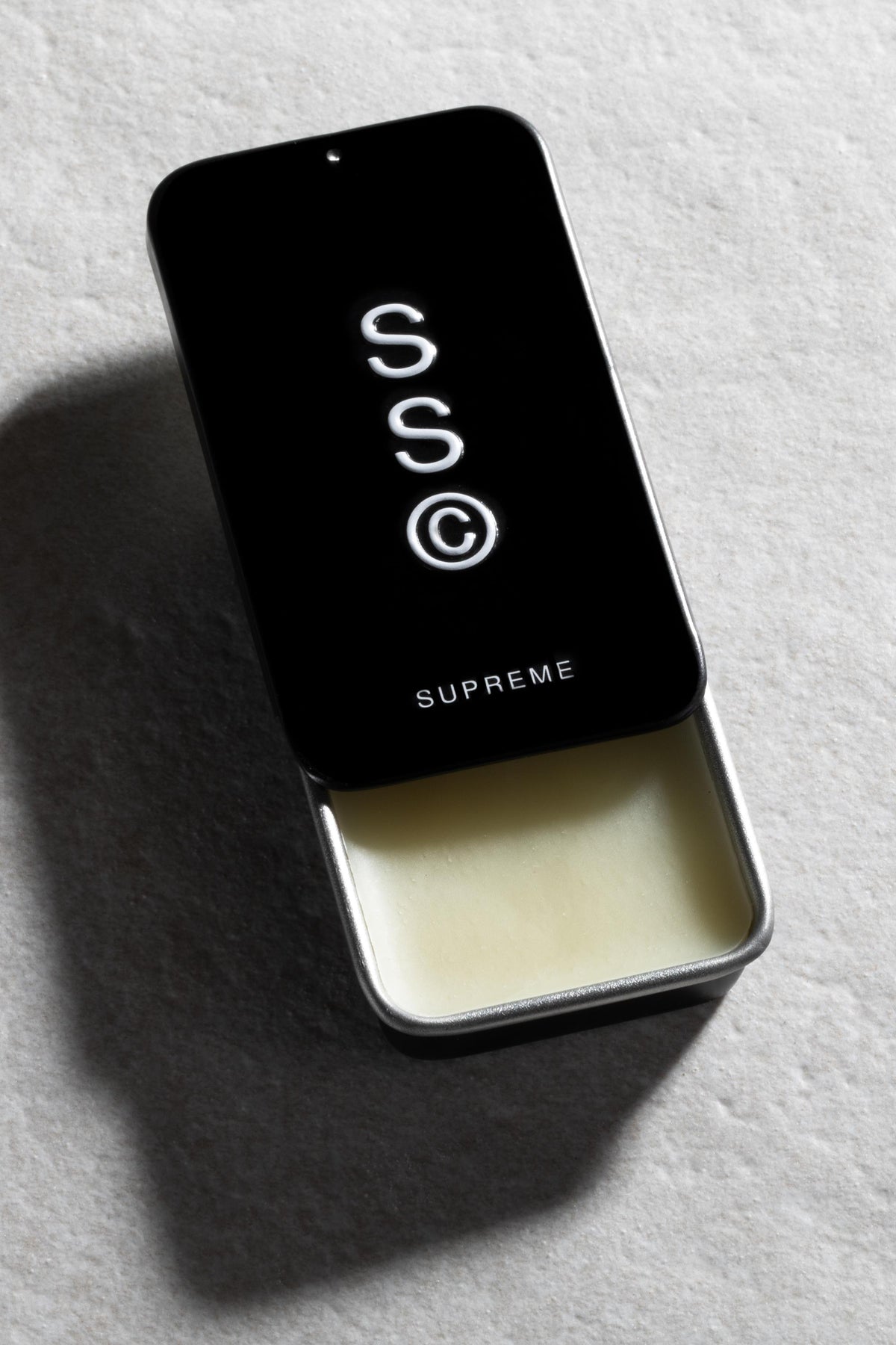 A compact Solid State - Supreme cologne tin rests on a lightly textured surface.