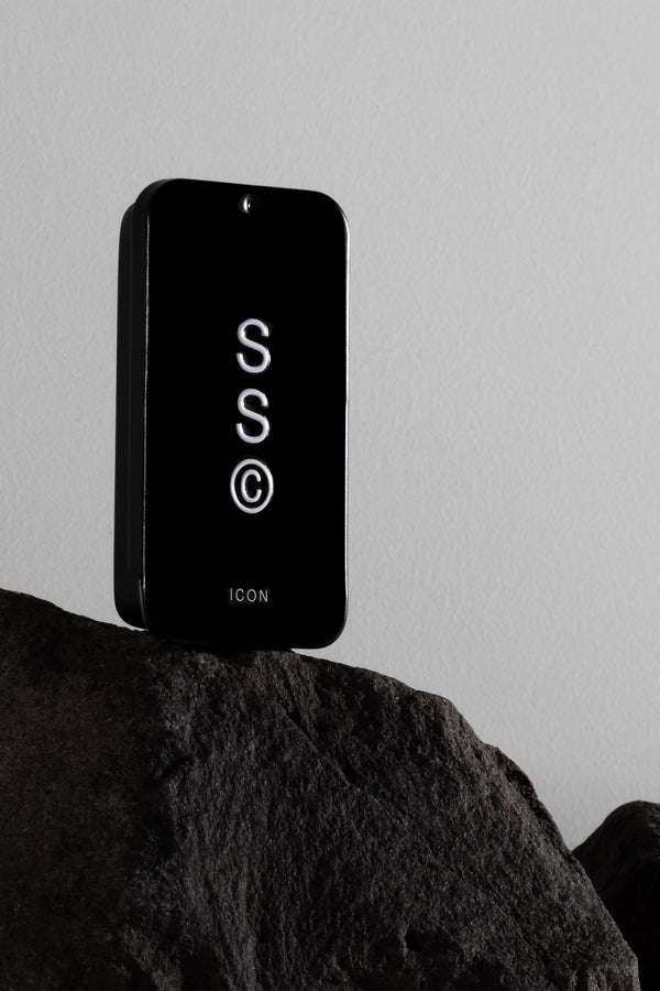 Solid State - Icon cologne sits on a dark rock with a plain light wall in the background.