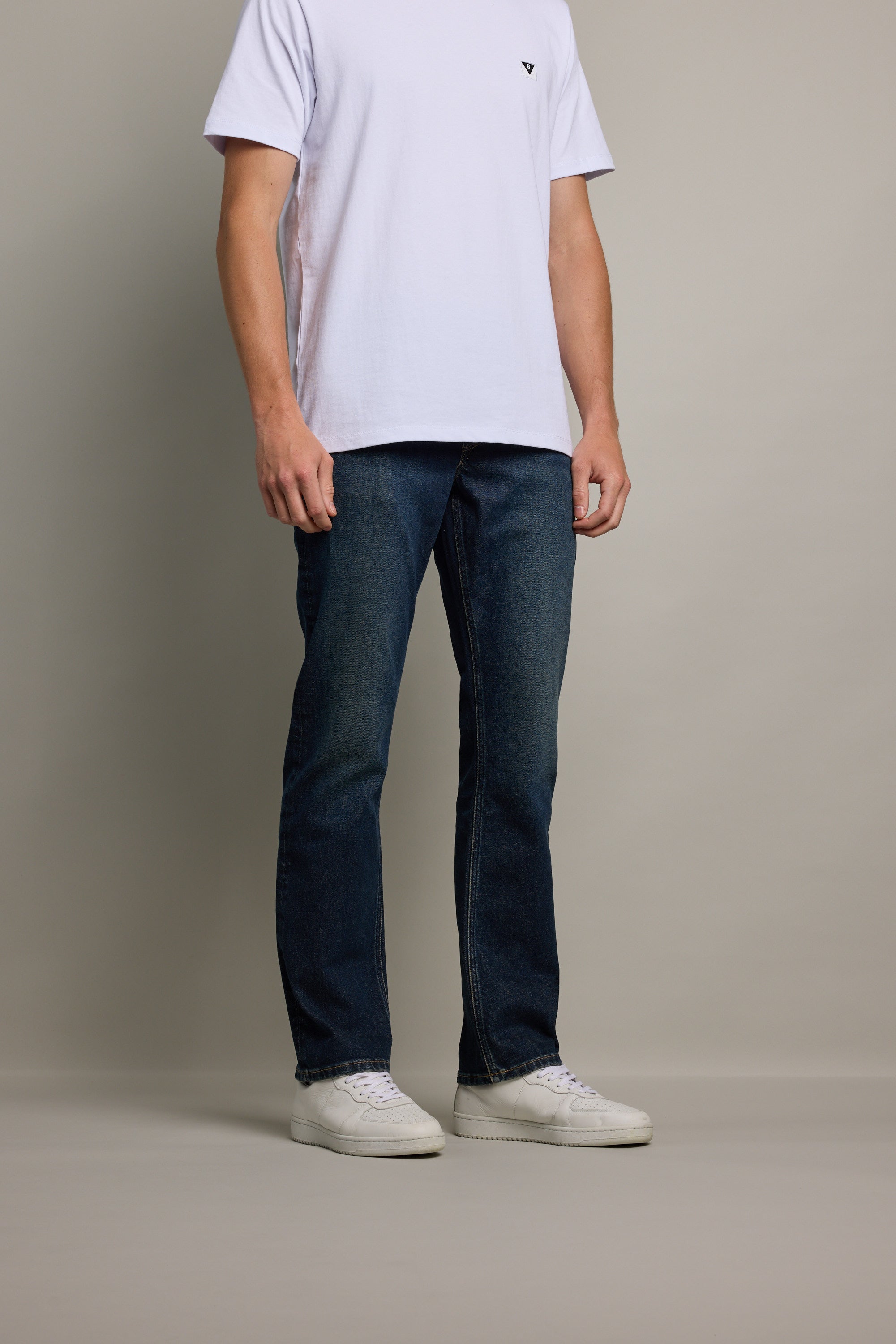 A person stands against a plain background, wearing a white t-shirt, Barkers Wanderer Denim Straight Jeans, and white sneakers. Their head is not visible in the image.