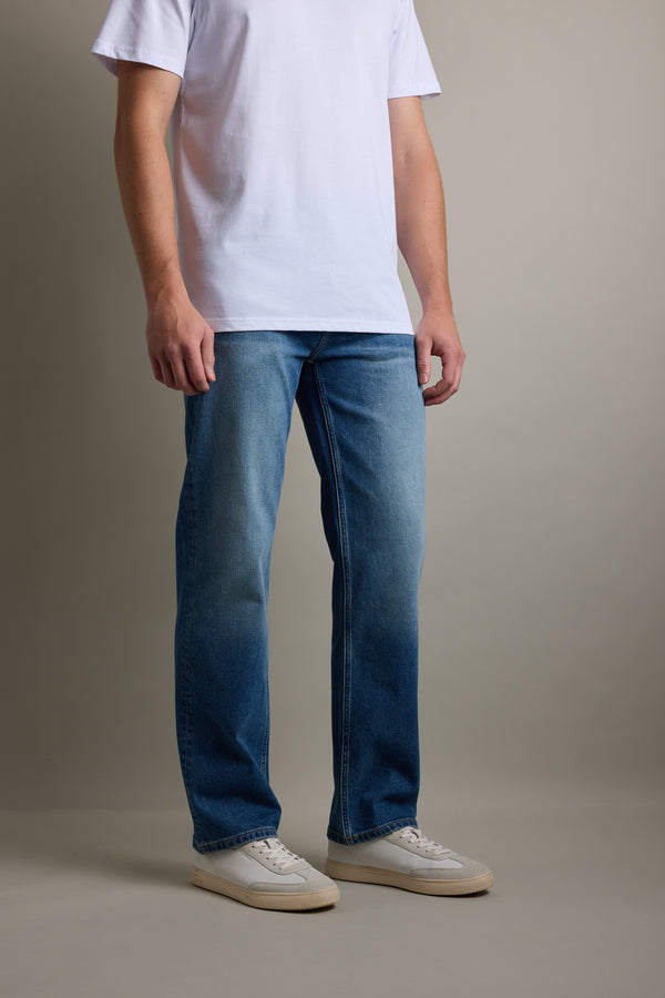 Wearing Barkers' Drifter Denim Relax Jean, white tee, and sneakers against a plain background.