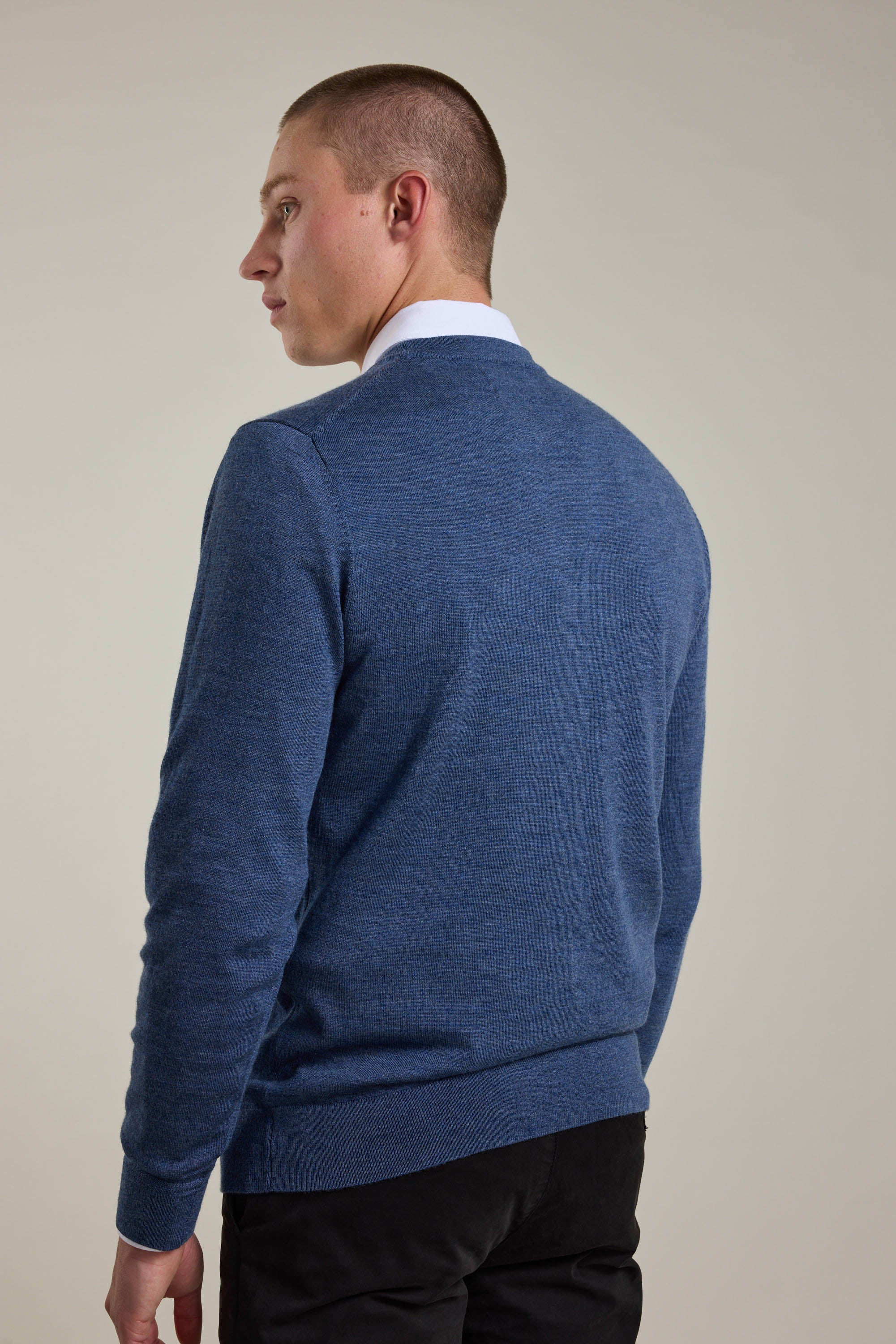 A man wears a Barkers Skyland ZQrx Merino Crew sweater—made from ethically sourced merino—standing against a plain light background, facing away while looking over his left shoulder.