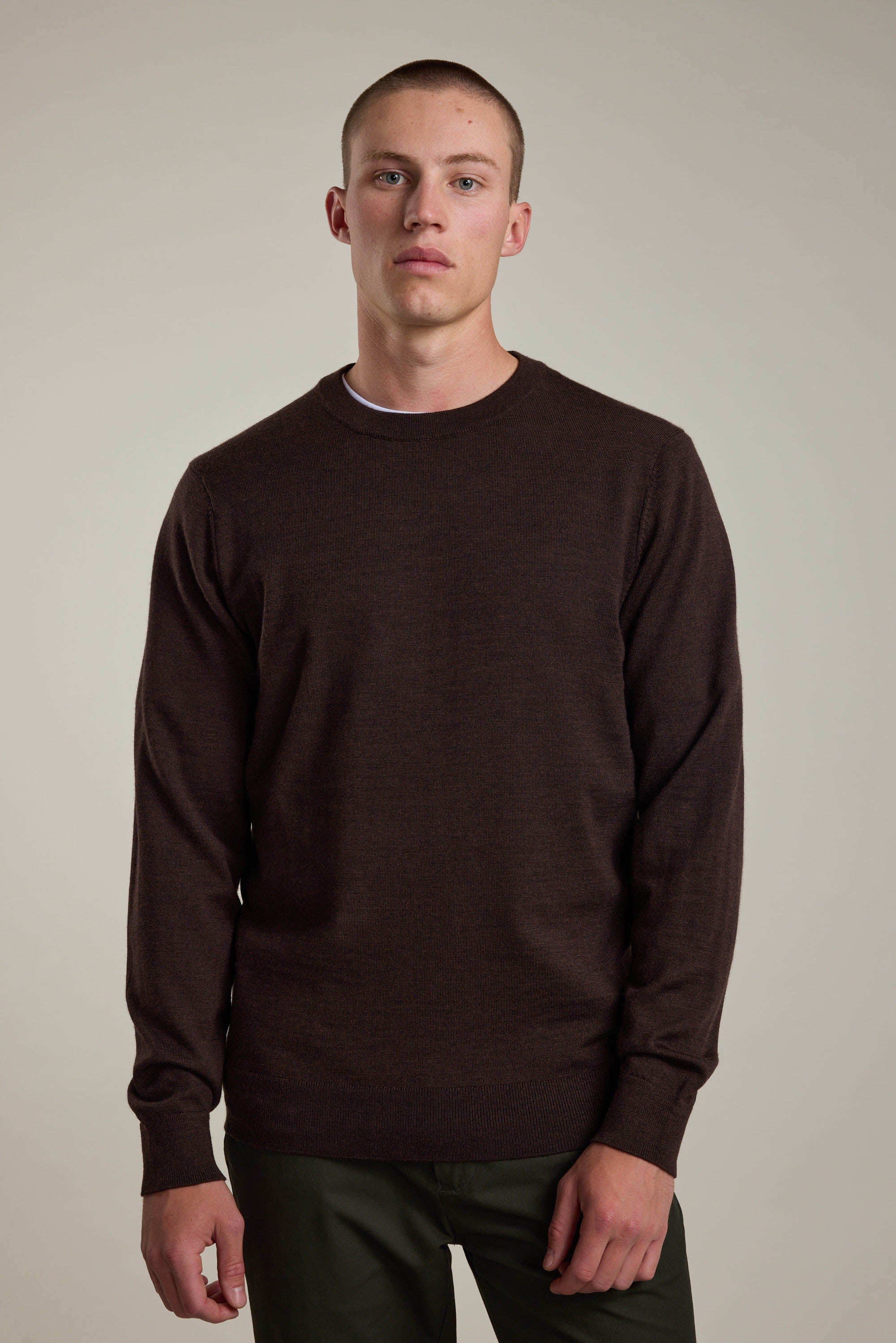 A man wears a plain dark brown long-sleeve Skyland ZQrx Merino Crew sweater by Barkers, standing facing forward against a neutral background with a neutral expression.