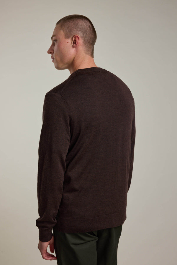 A person with short hair is seen from behind, wearing a dark brown Barkers Skyland ZQrx Merino Crew sweater made from sustainable New Zealand merino wool. The background is plain and light-colored.