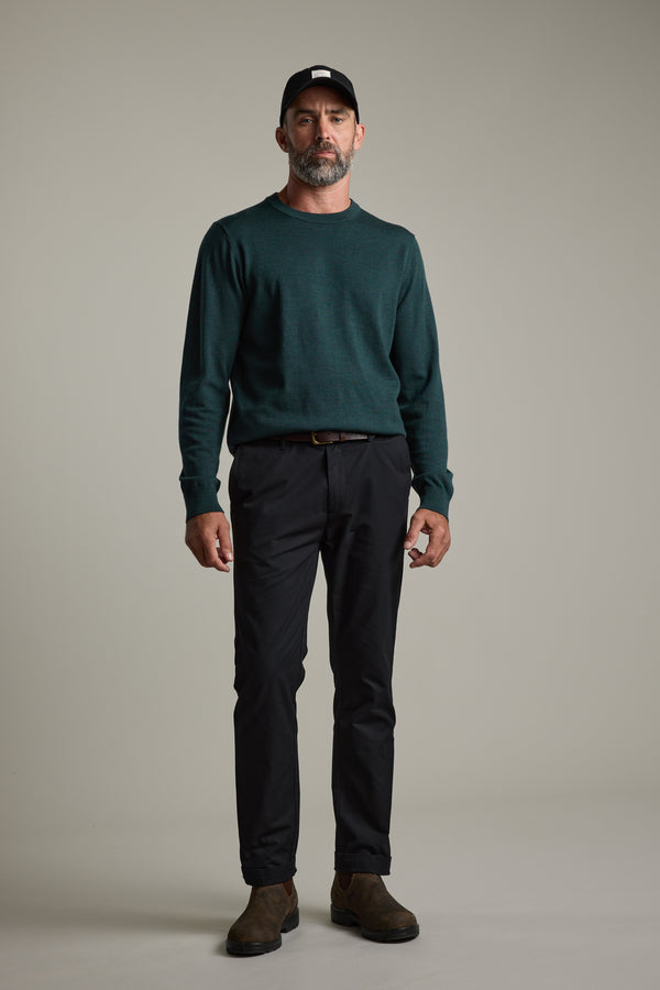 Man in Barkers Skyland ZQrx Merino Crew, black pants, and cap against a plain background.