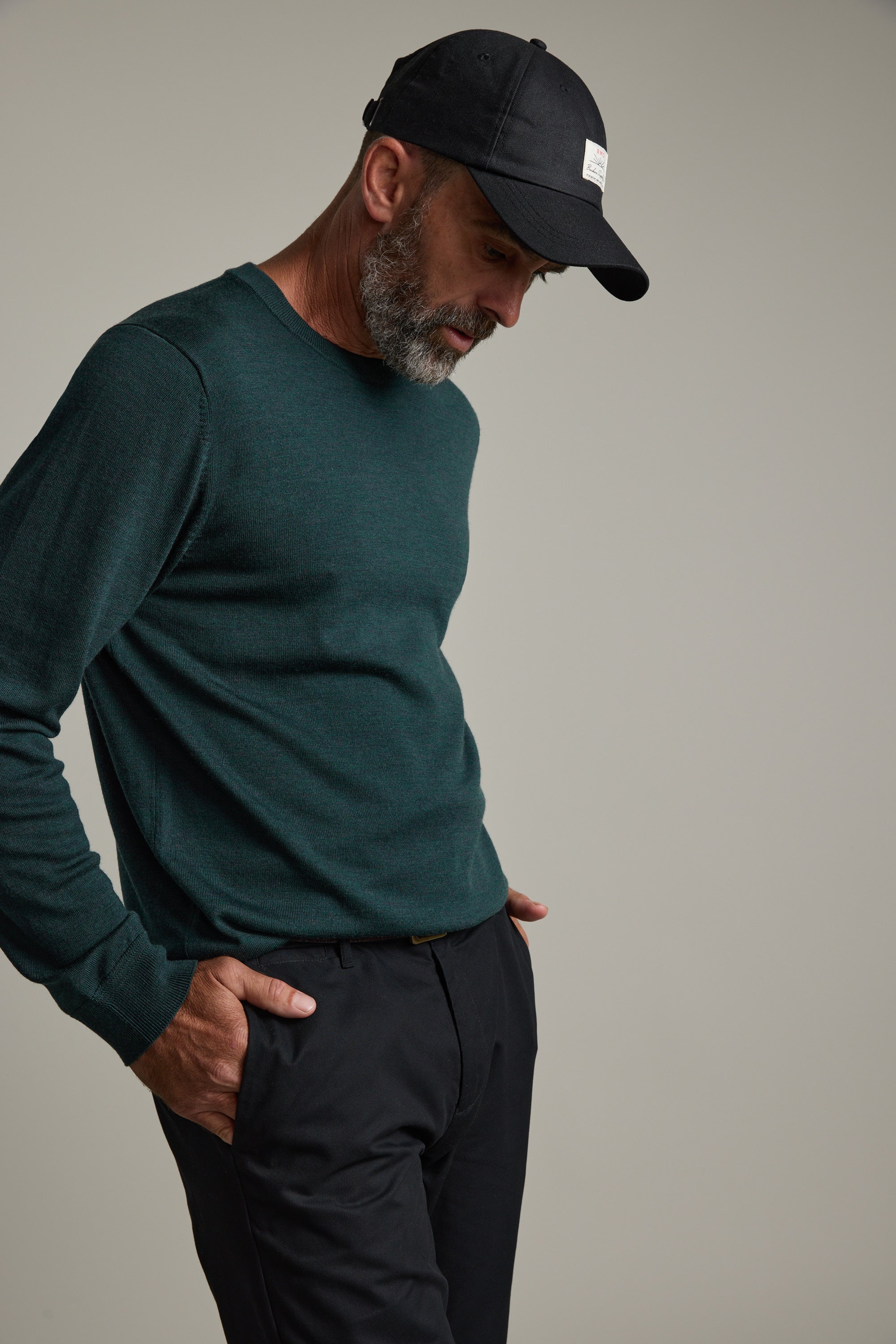 Man in green Barkers Skyland ZQrx Merino Crew and black cap, hand in pocket, plain background.