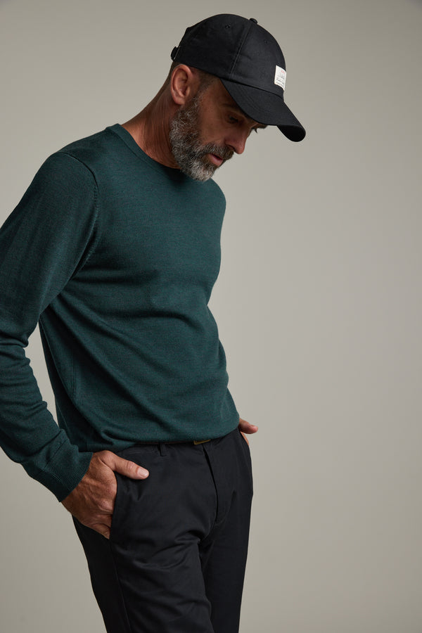 Man in green Barkers Skyland ZQrx Merino Crew and black cap, hand in pocket, plain background.