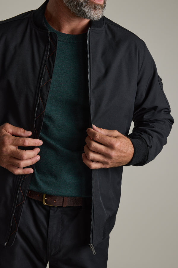 Man zipping up a black jacket over a green Barkers Skyland ZQrx Merino Crew shirt.