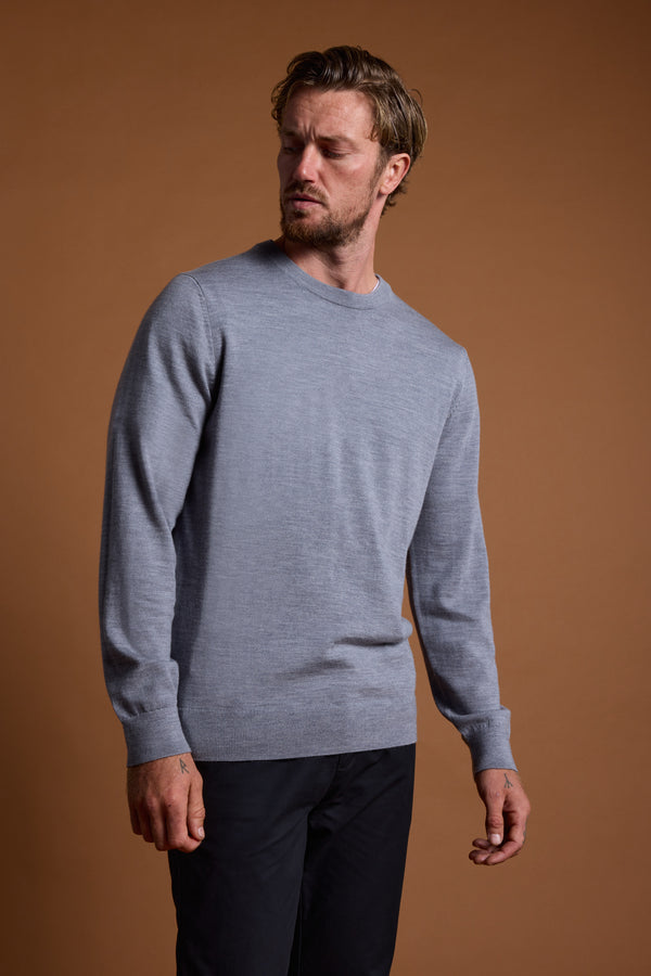 A man wearing the Barkers Skyland ZQrx Merino Crew in light gray and black pants stands against a plain brown background, looking down and slightly to his right with a neutral expression.