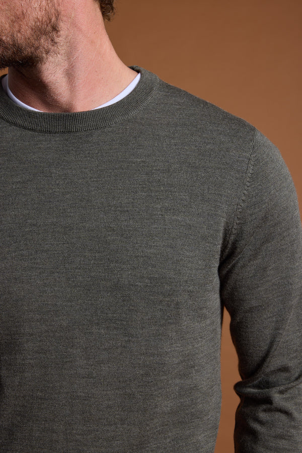 A close-up of a man wearing the Barkers Skyland ZQrx Merino Crew in dark green over a white tee, shown shoulder to mid-torso against a plain brown background, with his face partly out of frame.