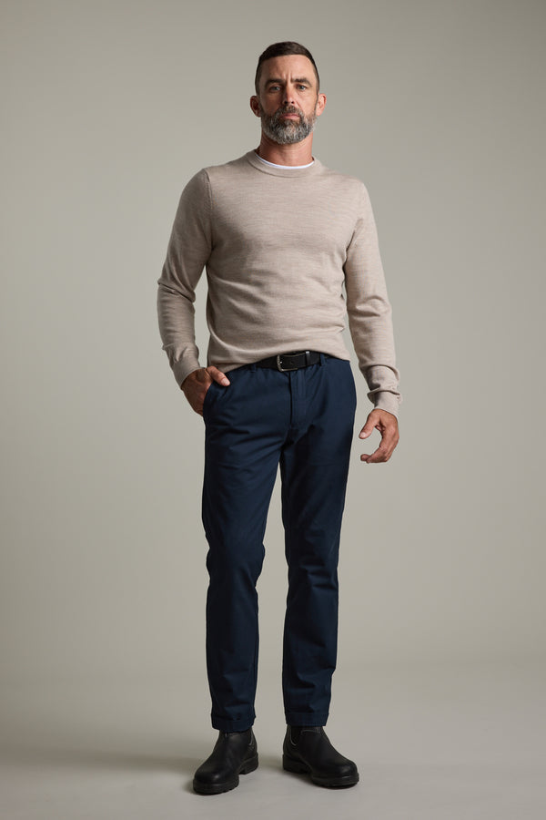Man in a beige Barkers Skyland ZQrx Merino Crew, navy pants, and black boots on plain background.