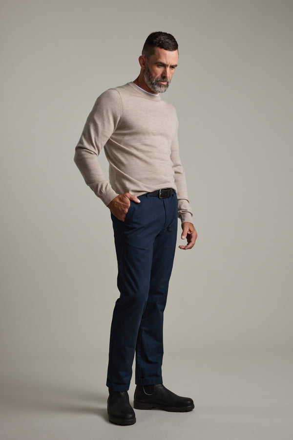 Man in beige Skyland ZQrx Merino Crew by Barkers and navy pants against a plain gray background.