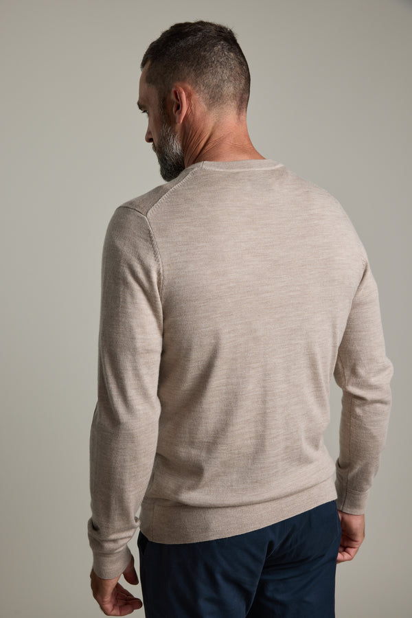 A man in a beige Barkers Skyland ZQrx Merino Crew and dark pants stands against a plain background.